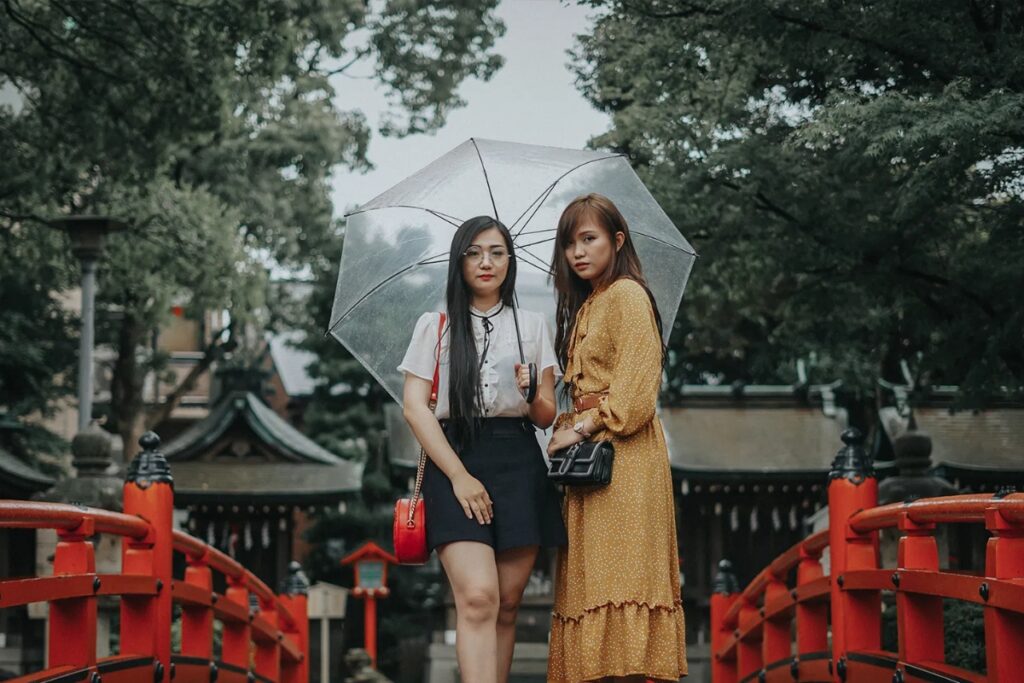Fashionable models posing with an umbrella against a Japanese shrine bridge in Tokyo