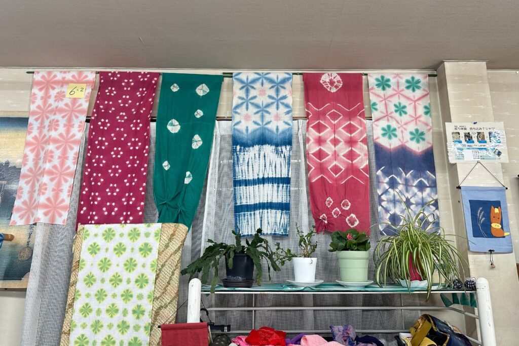 Vibrant colored textile masterpieces with intricate white patterns hanging on display inside a heritage workshop during an Arimatsu Shibori tie-dyeing class.