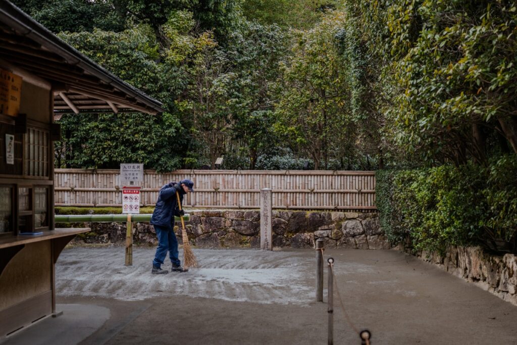 A traditional gardener meticulously raking the gravel to maintain zen sand patterns at Ginkaku-ji, an educational stop on our Kyoto private culture tour.