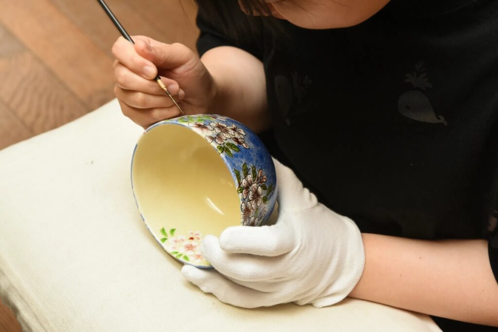 An artist delicately applying fine brushwork to a beautiful cherry blossom ceramic bowl during a Kyoto pottery workshop experience.