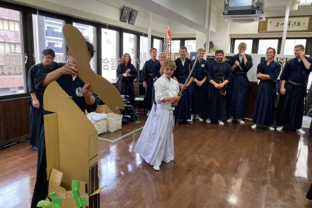 Young guest performing the cutting trial on a carton target as the group watches at a Tokyo Iaido experience