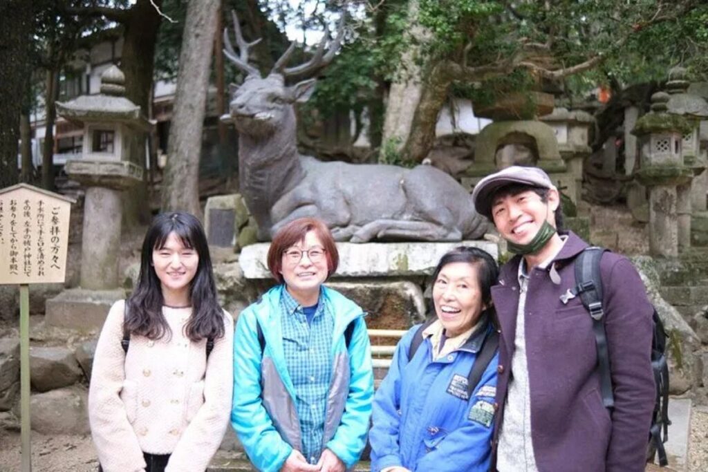 Three smiling friends posing next to a carved stone deer monument in the forest
