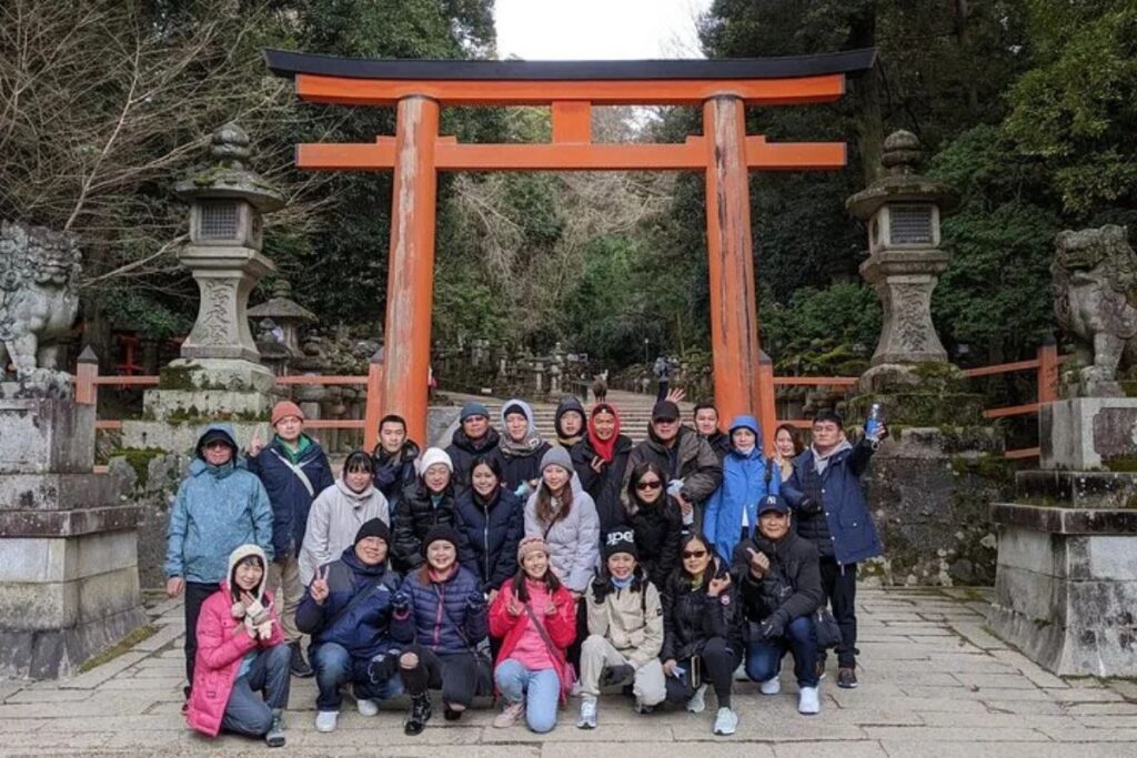 A large group of travelers posing in front of a giant red Torii gate during a shared Nara bike tour.