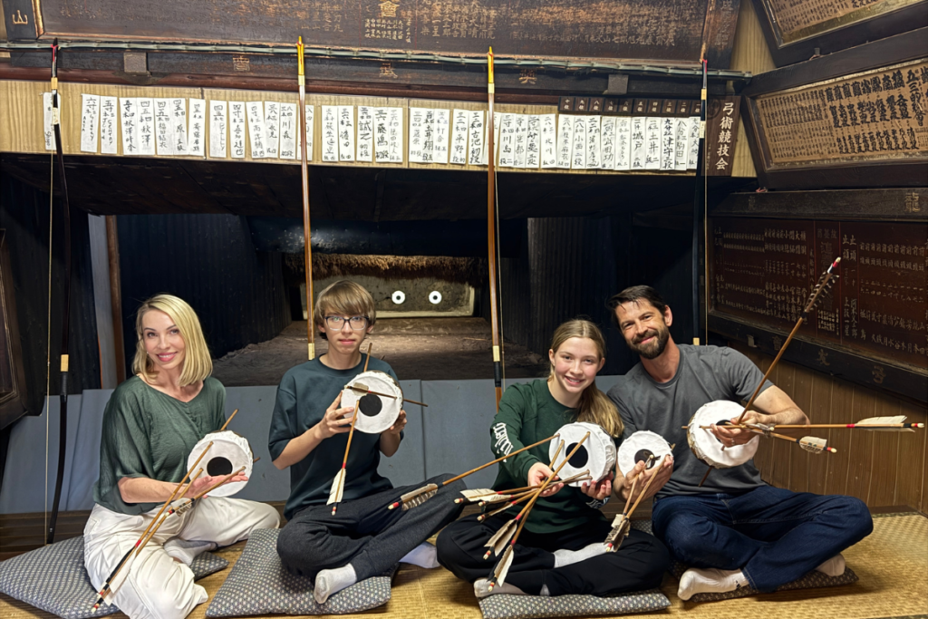 A group of travelers holding archery targets and arrows inside a traditional 160-year-old Kyudo dojo during an authentic seated archery experience in Kyoto.