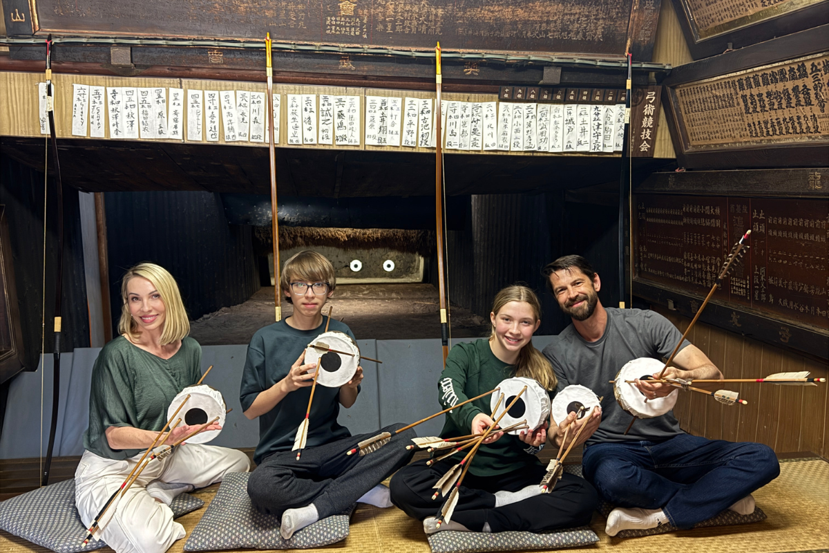 A group of travelers holding archery targets and arrows inside a traditional 160-year-old Kyudo dojo during an authentic seated archery experience in Kyoto.
