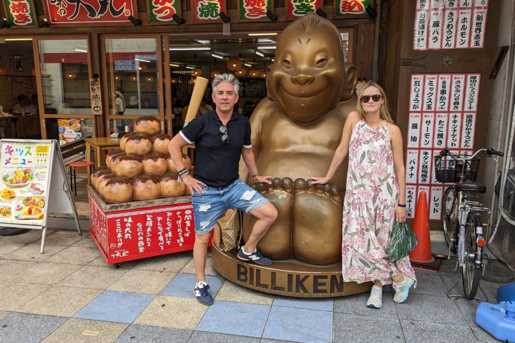 A smiling couple posing next to a famous golden lucky statue on a sunny day.