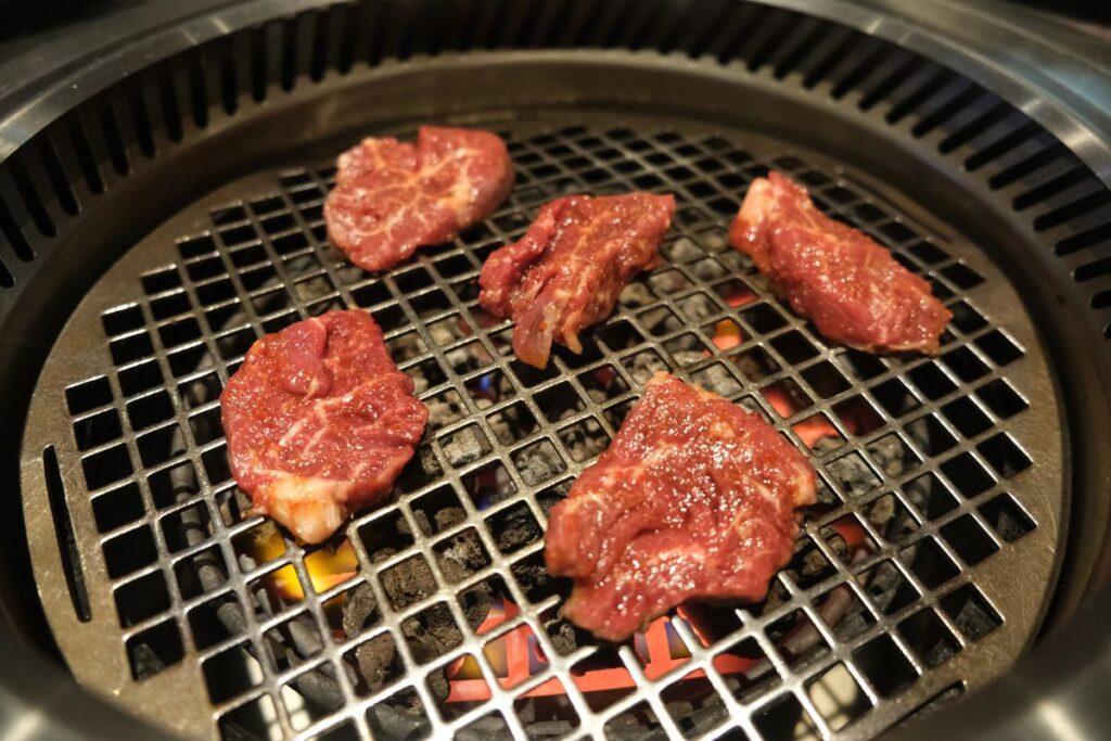 Fresh slices of raw meat cooking on a hot charcoal barbecue grill.