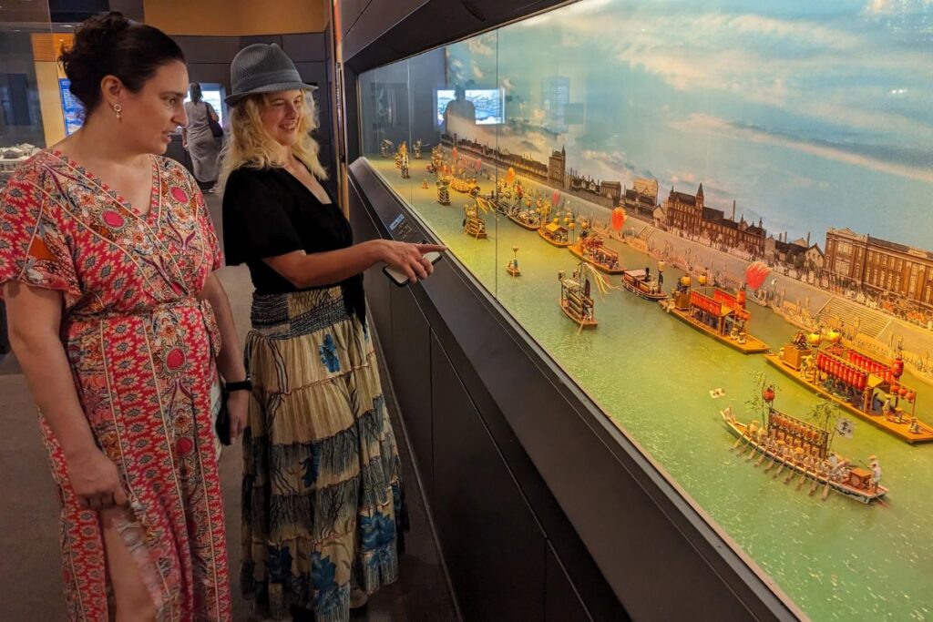 Two women admiring a detailed miniature city diorama inside a cultural exhibit.
