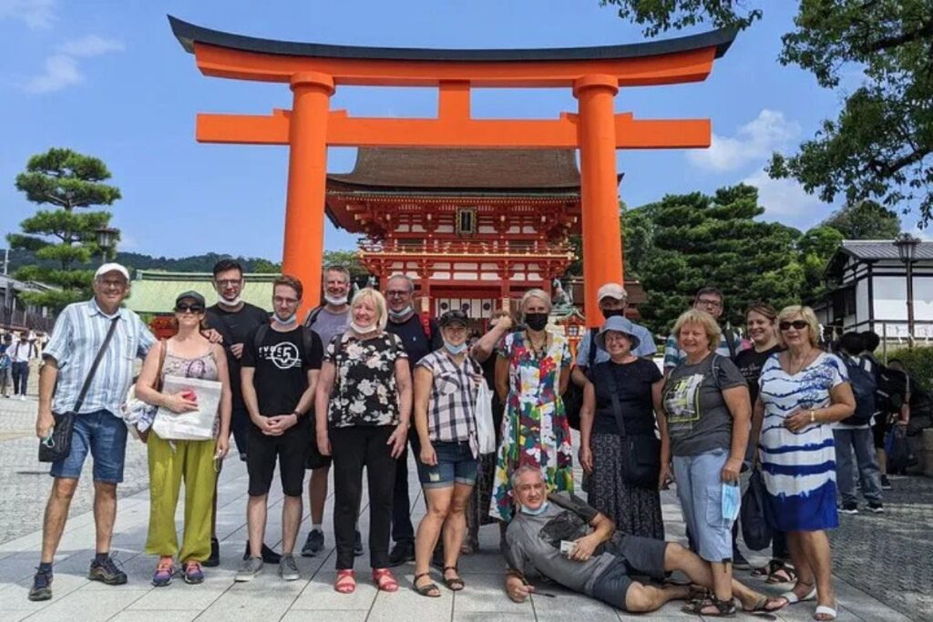 A large group of travelers posing in front of a giant red shrine gate.