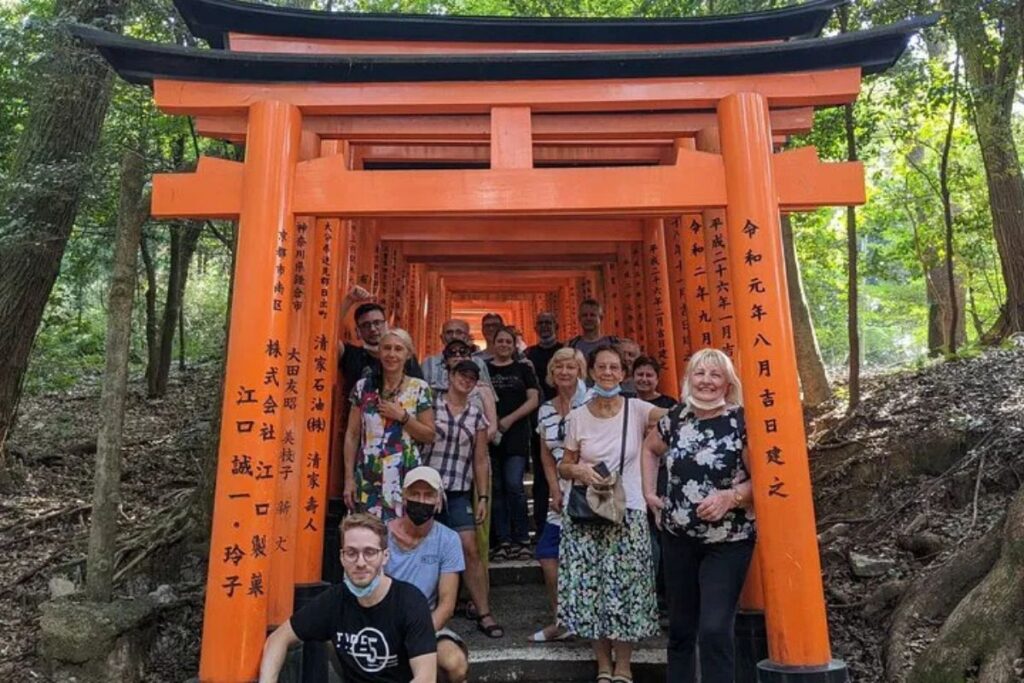 Travelers posing inside a tunnel of orange shrine gates during a Kyoto Fushimi food tour.