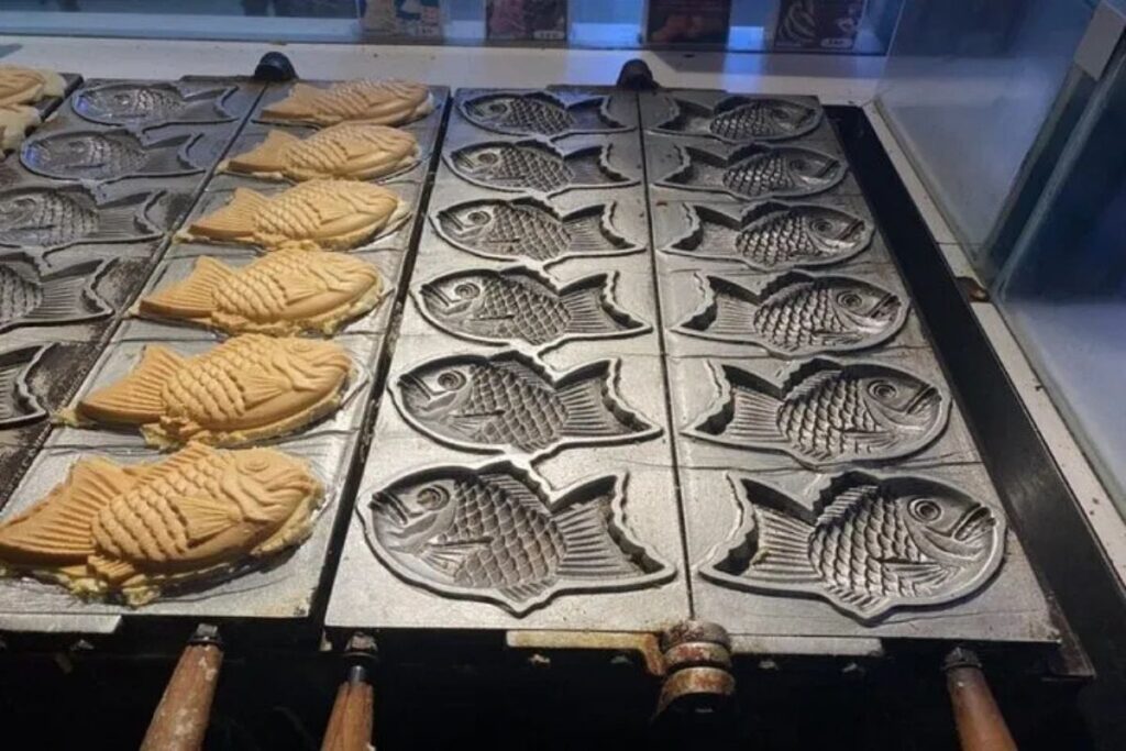 Fish shaped waffles filled with sweet bean paste cooking in an iron mold.
