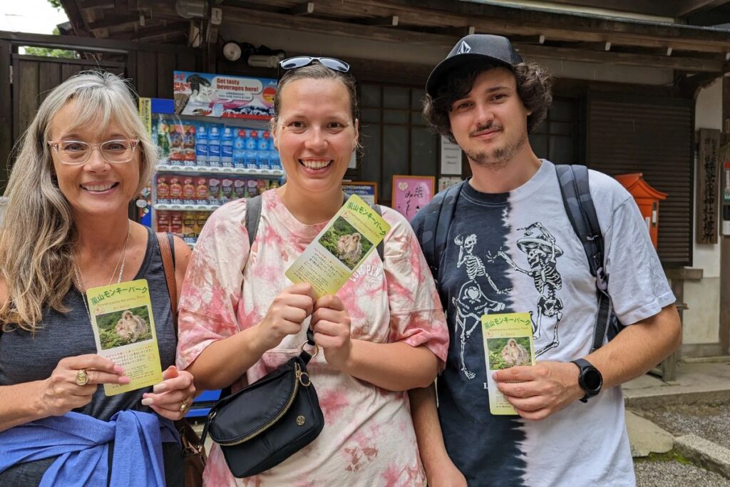 Three smiling travelers holding up their admission tickets outside a local nature park.
