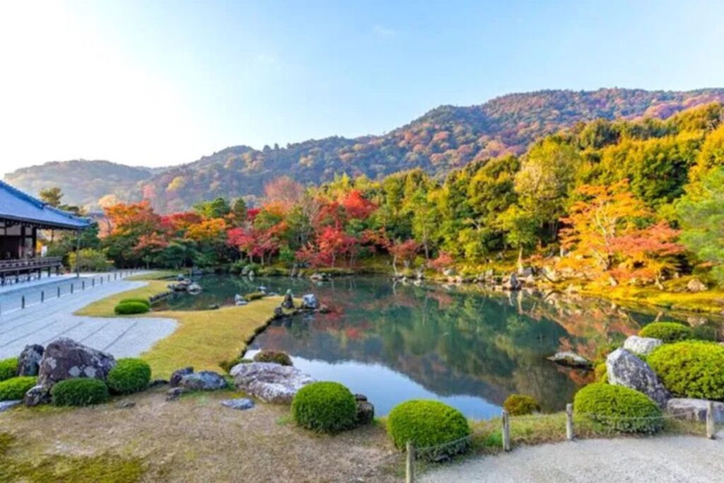 A tranquil traditional Japanese garden featuring a clear pond surrounded by colorful autumn trees.