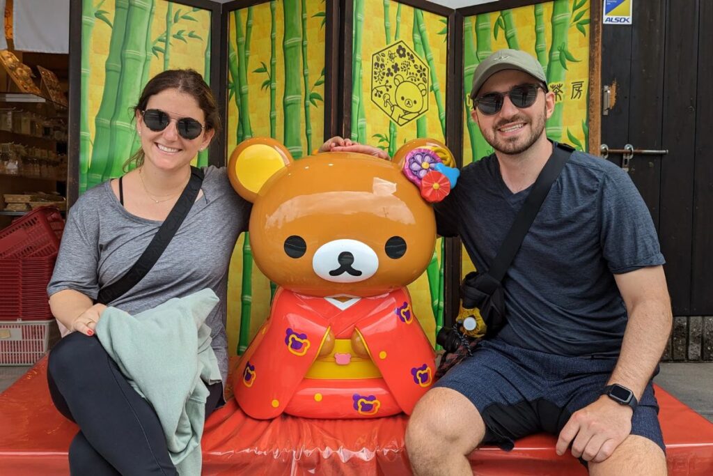 A couple smiling next to a cute mascot character statue on a private arashiyama walking tour.