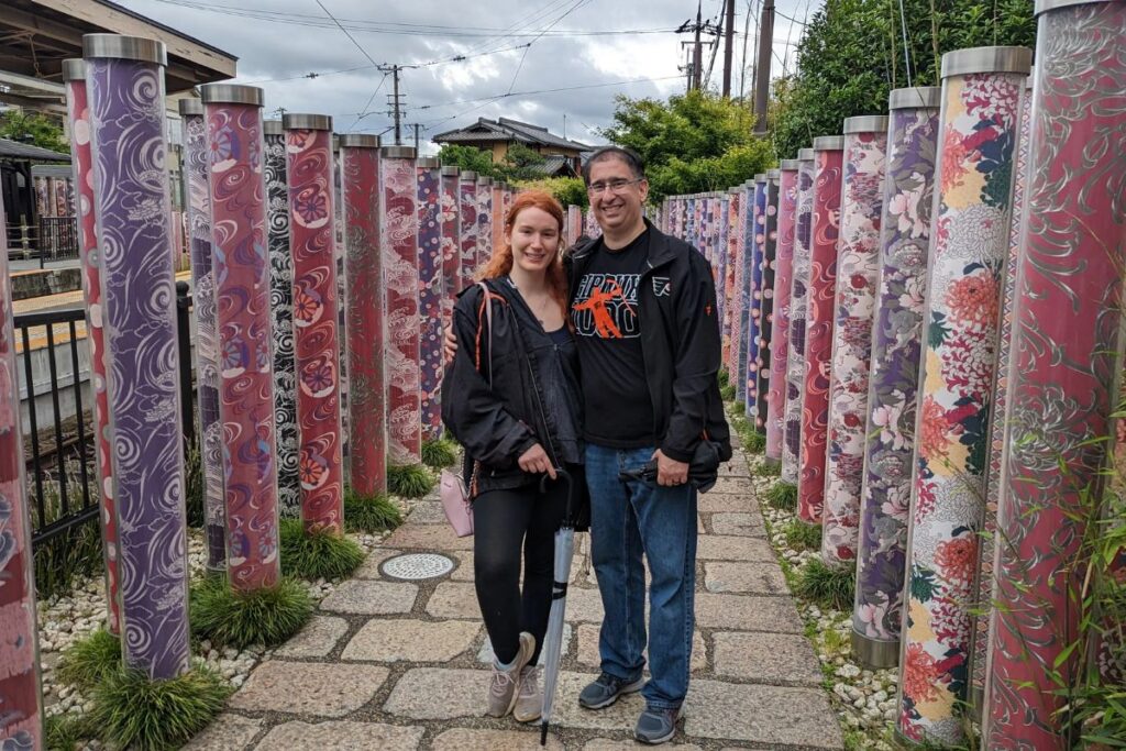 A smiling couple standing between beautiful pillars decorated with colorful traditional fabric patterns