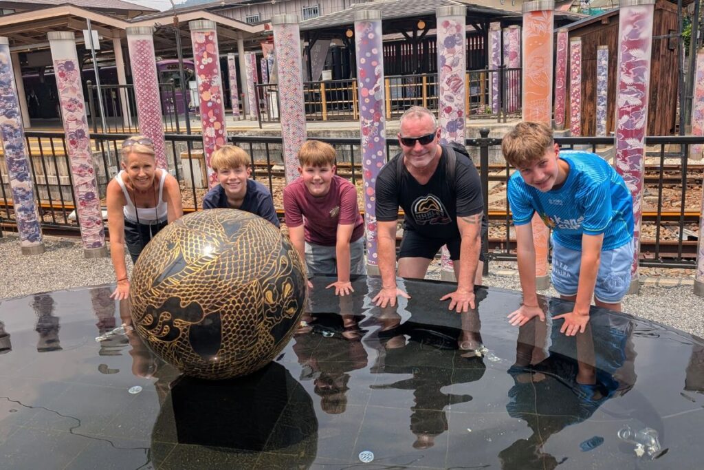 A happy group of five posing around a decorative black and gold sphere with colorful pillars behind them.