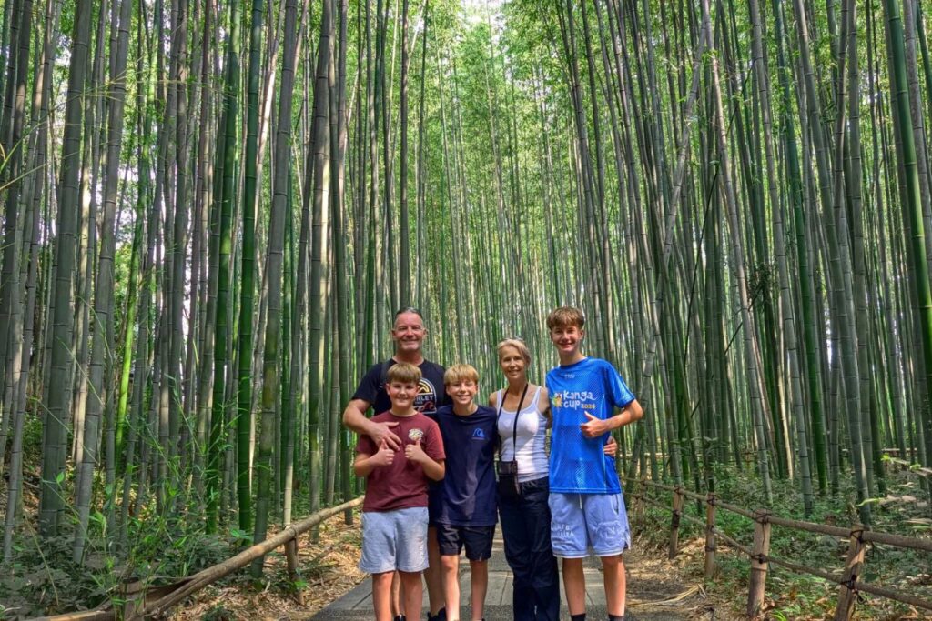 A family posing together in a lush green bamboo grove during a shared arashiyama walking tour.