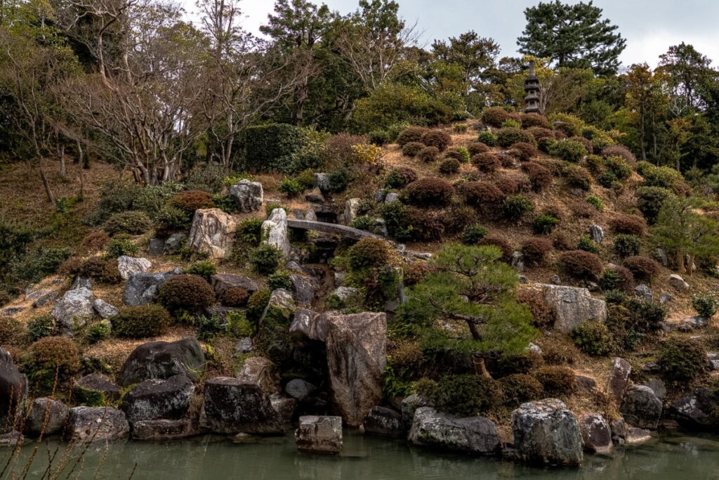 A traditional Japanese hillside garden featuring sculpted bushes, stone steps, and a distant pagoda tower, viewed during a scenic Kyoto private culture tour.