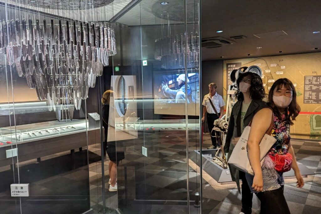 Visitors admiring a massive chandelier made entirely of shiny steel blades inside a local craft museum.