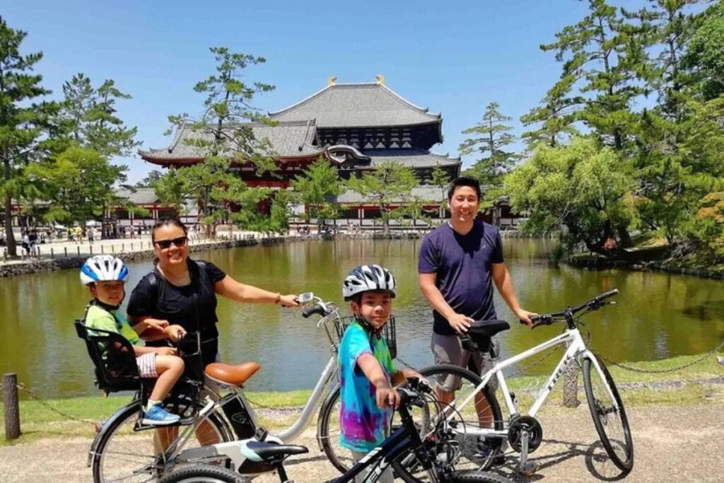 A family enjoying a private nara e-bike tour along a scenic pond with a massive traditional temple landmark in the background.