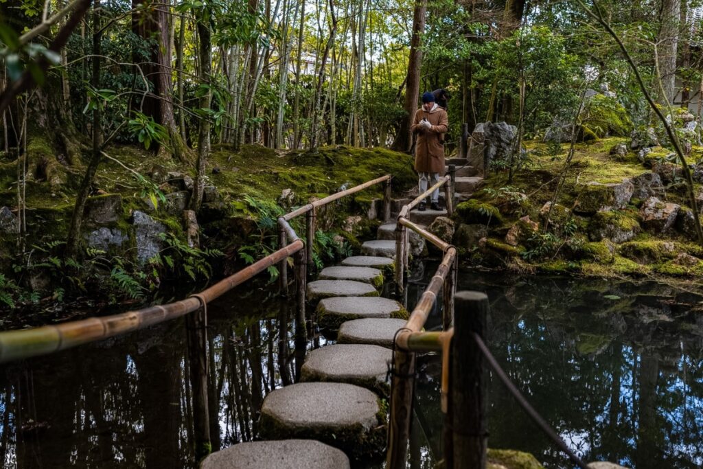 A guest gracefully walking along a curved path of rhythmic stepping stones across a pond during an exclusive Kyoto private culture tour.