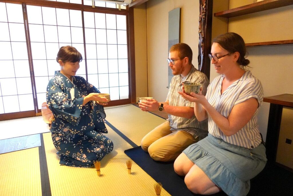 A guide in a blue kimono serving a couple during a private Kyoto Machiya tea ceremony.