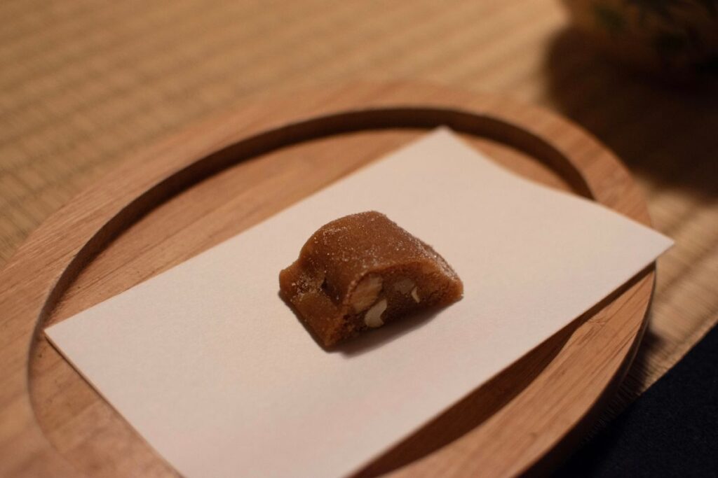 A small traditional Japanese sweet resting on a piece of white paper over a wooden serving tray.