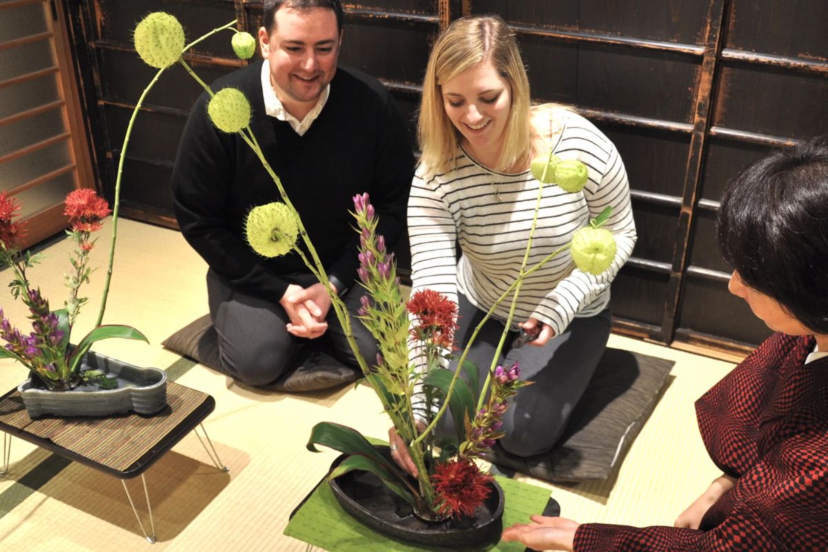 A smiling couple designing a beautiful botanical art piece under the guidance of a local teacher during a Kyoto Machiya Ikebana class.