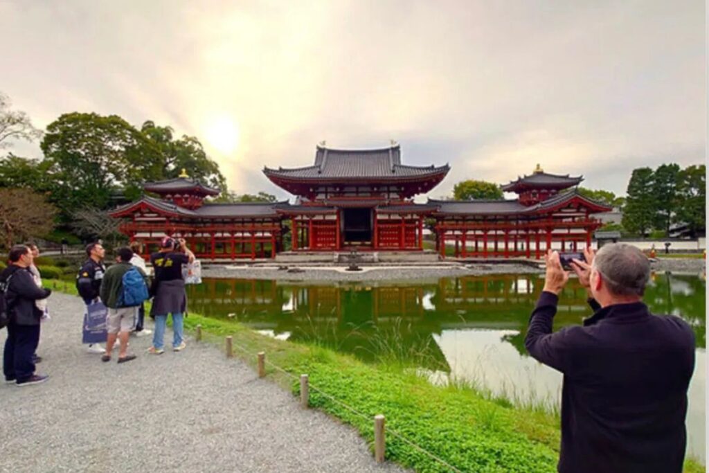 Visitors taking photos of a magnificent red historic temple building reflecting beautifully in a calm pond during Uji culture bike tour.
