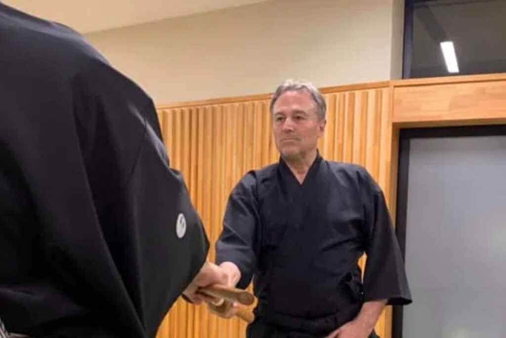 Iaido instructor handing a practice sword to a guest in a traditional dojo in Tokyo