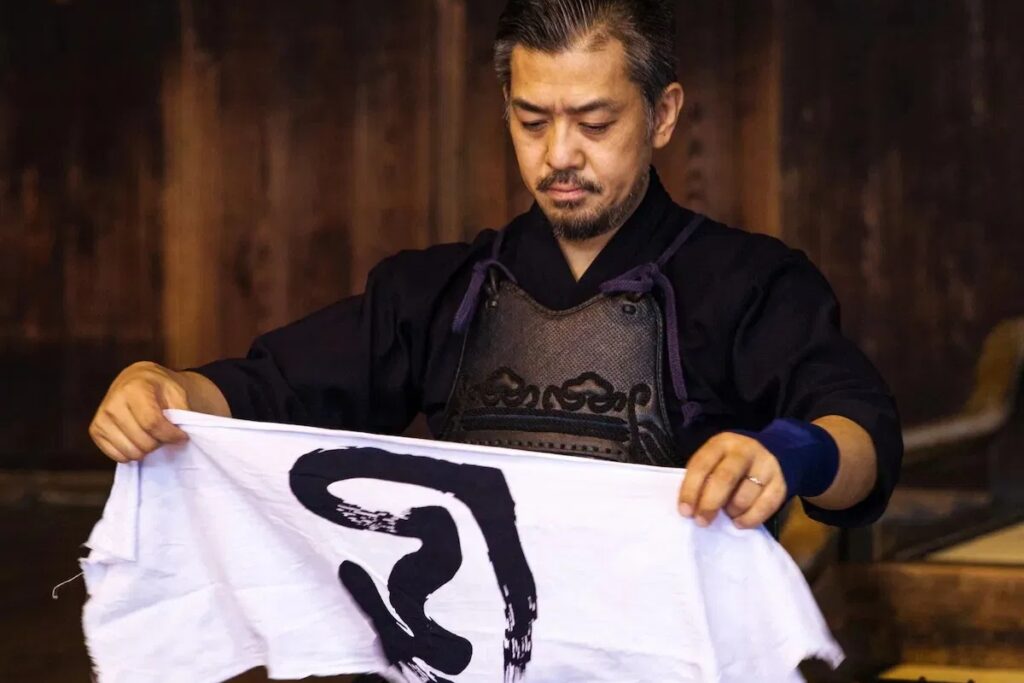 Master instructor Tomoyoshi holding a calligraphy tenugui during the Kendo experience in Kyoto