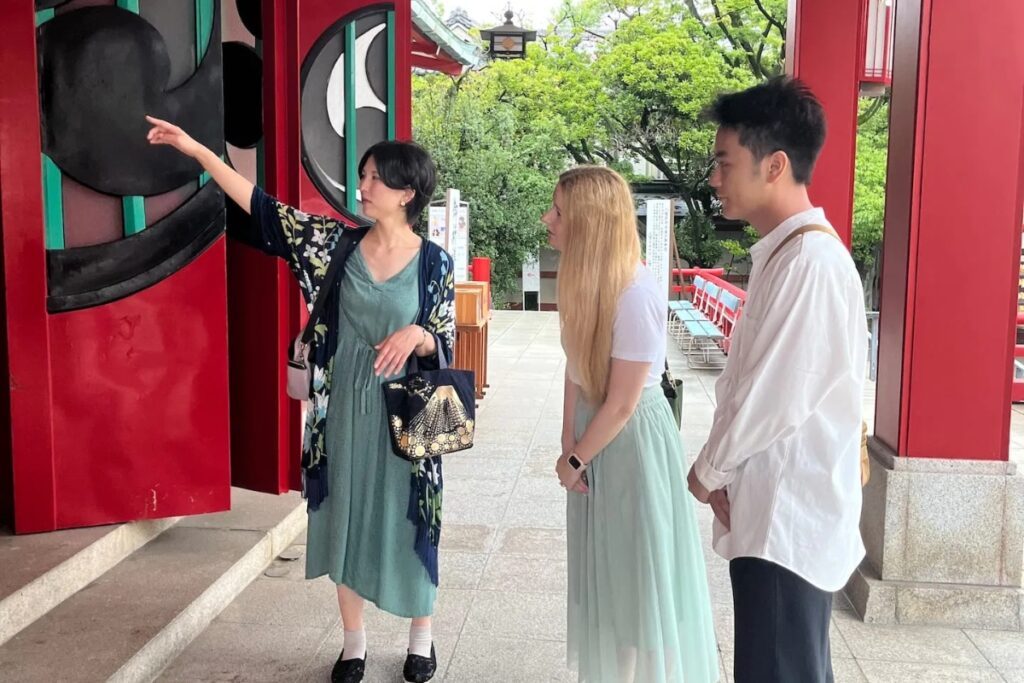 Local guide explaining the iconic black mitsudomoe crest at Tomioka Hachimangu Shrine in Tokyo
