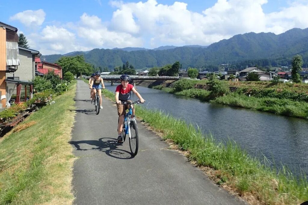 Cyclists riding along a peaceful paved path next to vibrant Satoyama rice paddies.