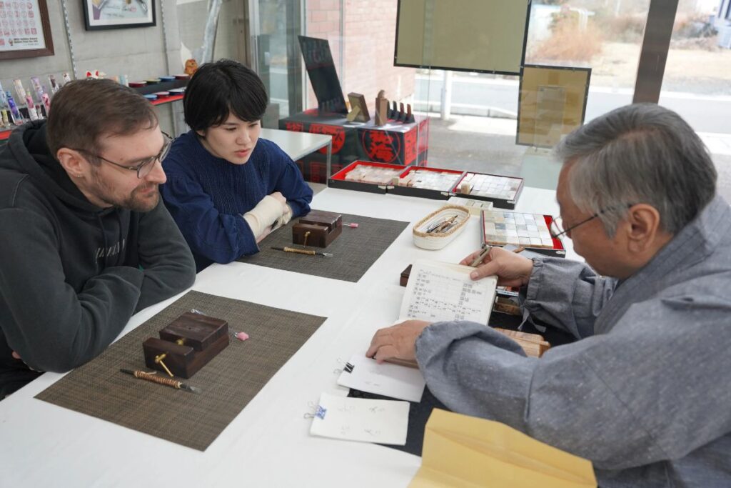 Guests and master artisan gathered around a workshop table to plan custom seal designs