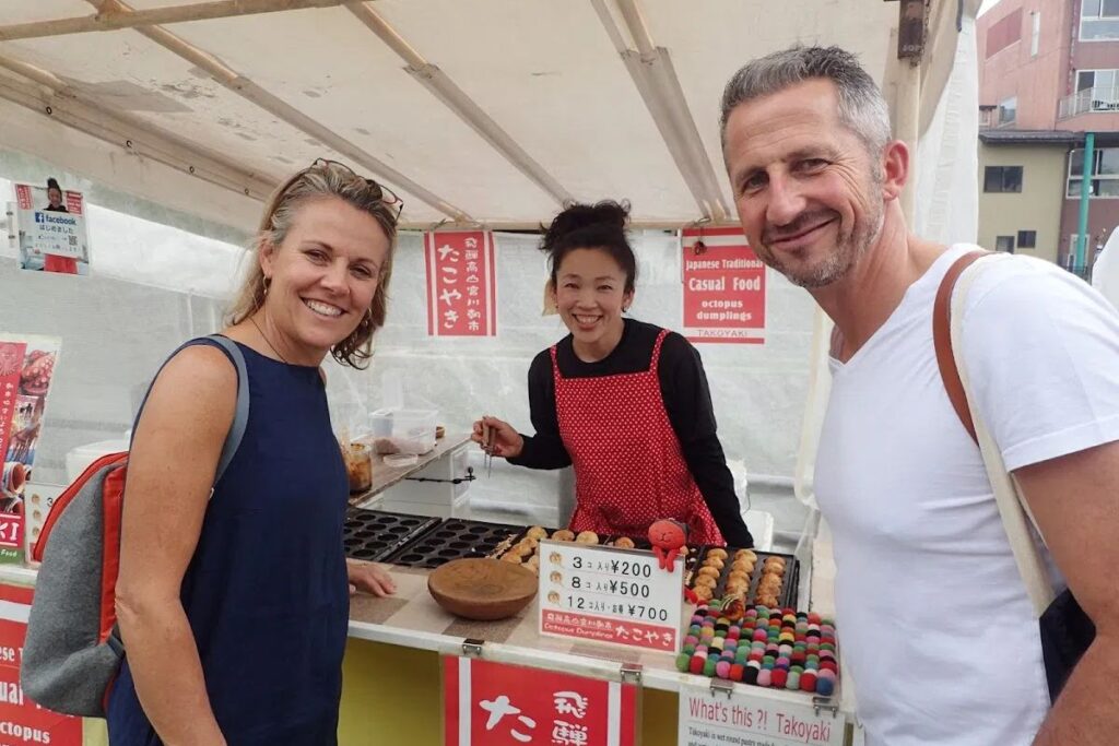 Guests interacting with a local food vendor at a morning market stall during an authentic Takayama food tour.