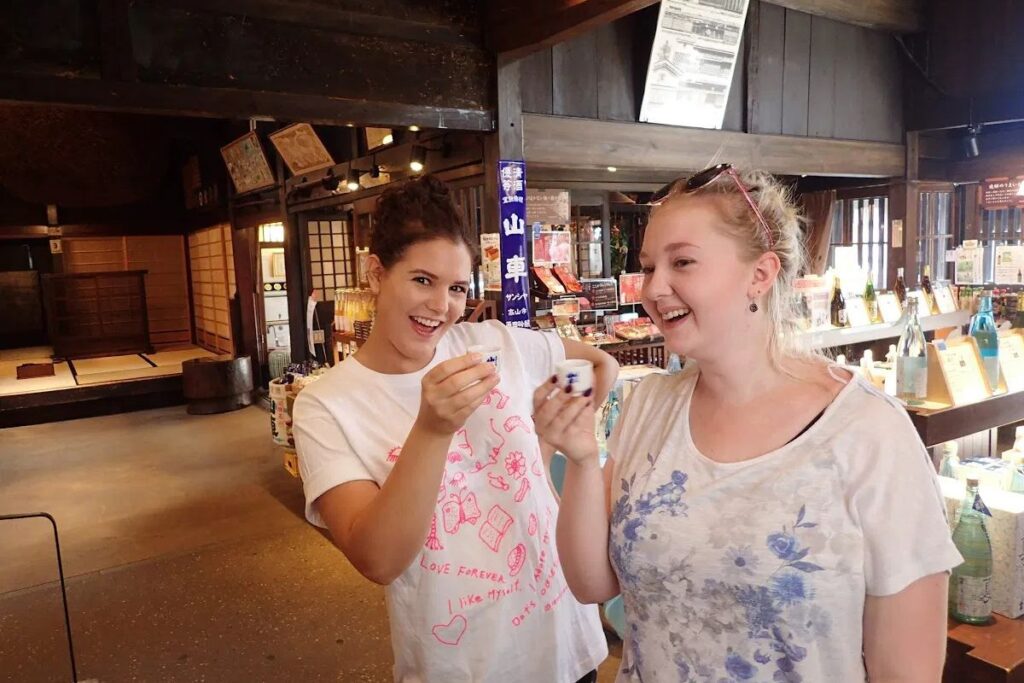 Two smiling travelers sampling regional delicacies and treats inside a traditional Japanese shop.