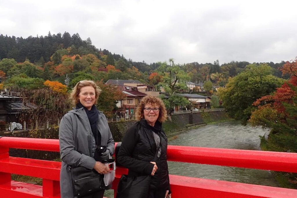Visitors standing on the iconic red Nakabashi Bridge overlooking the Miyagawa River in Takayama.