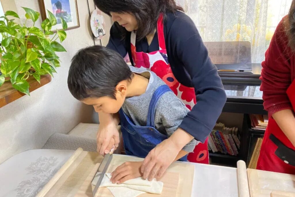 Local teacher guiding a child to cut udon noodles with a special knife in a Tokyo home kitchen