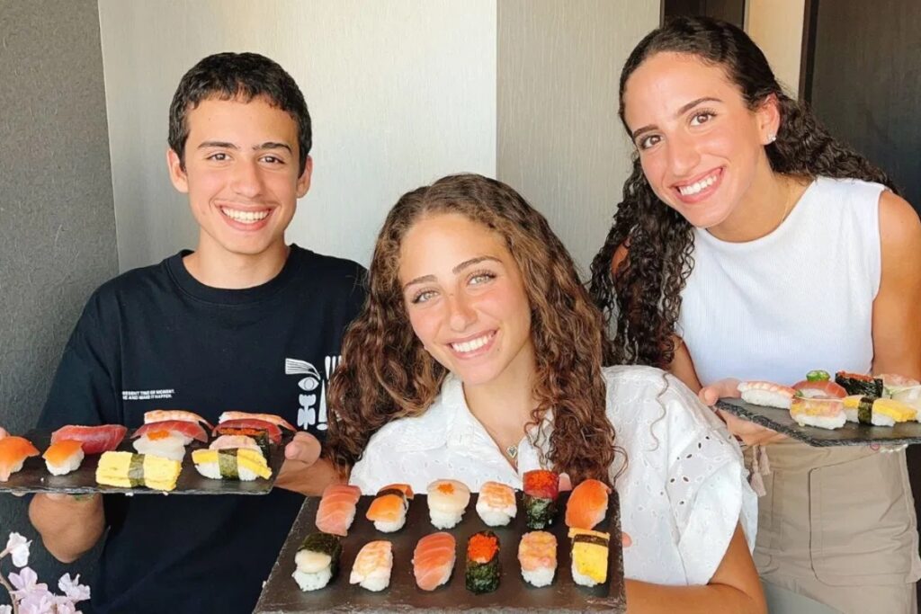 Three smiling guests proudly holding their finished sushi platters at an Asakusa class in Tokyo