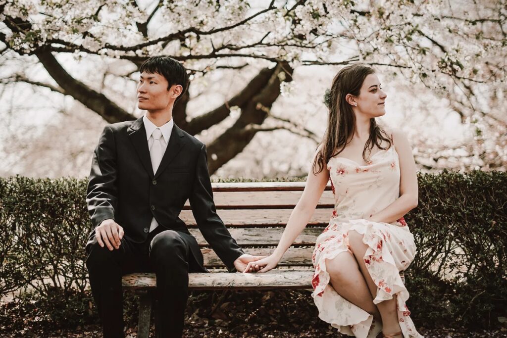 Couple holding hands on a bench beneath cherry blossoms captured by a Tokyo private photographer