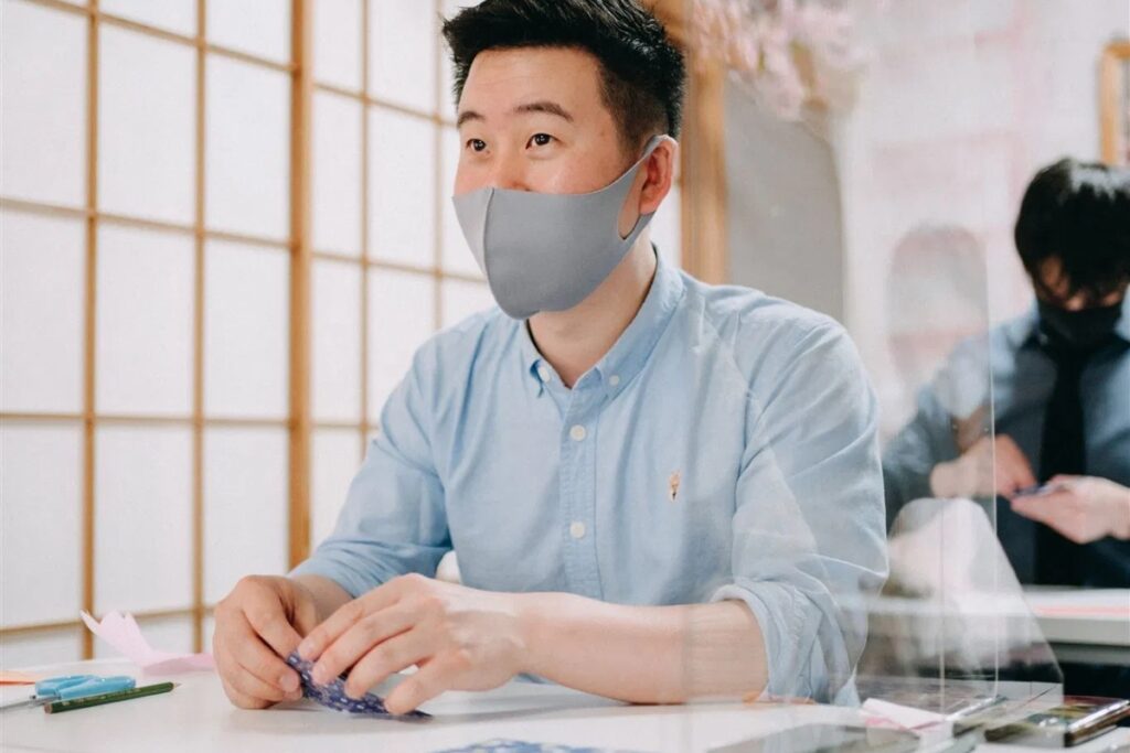 A male student focusing on folding premium patterned paper under the patient guidance of an instructor at a Tokyo origami private workshop.