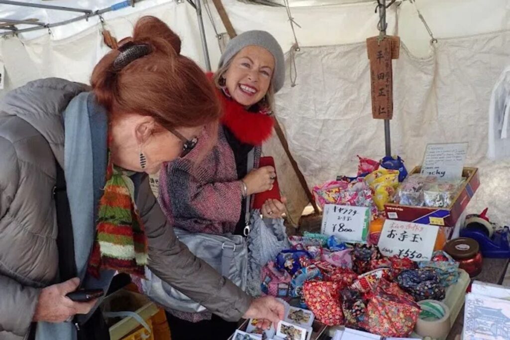 Travelers browsing fresh produce and homemade crafts at a bustling morning market on a Takayama food tour.