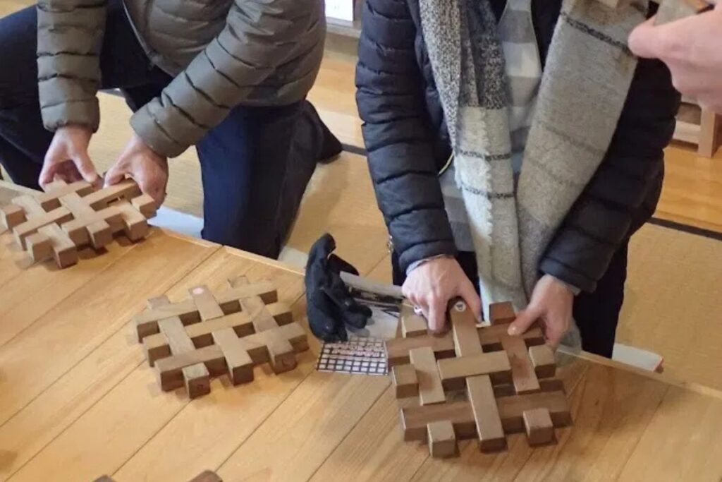 Hands assembling an intricate interlocking woodwork lattice design, showcasing ancestral Hida woodworking secrets.