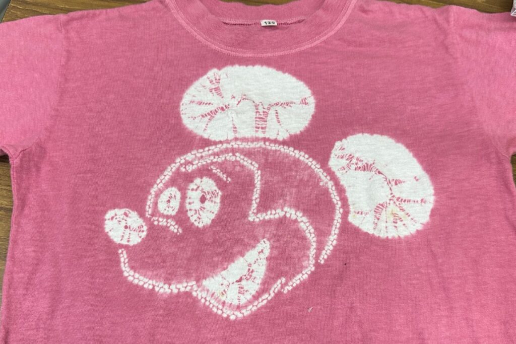 A custom pink t-shirt featuring a white cartoon mouse face design made through traditional coloring methods.