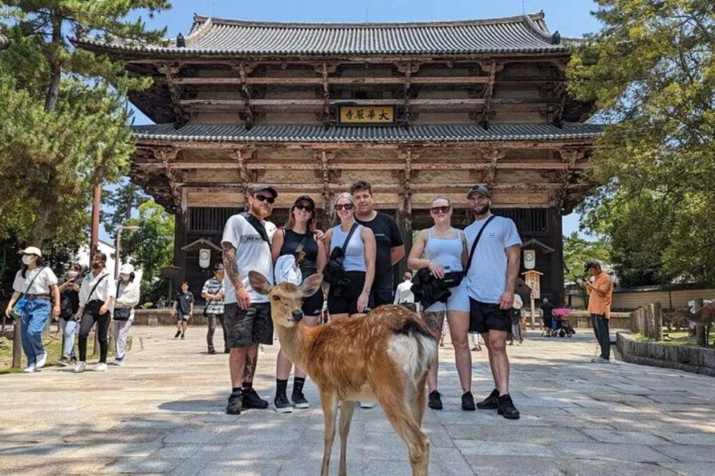 A group standing with a local deer in front of a historic temple gate during a Nara family bike tour.