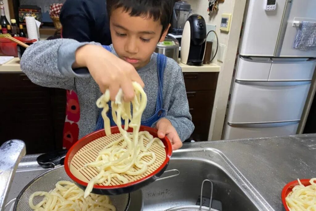 Young guest rinsing freshly boiled udon noodles in a colander during a Tokyo cooking class