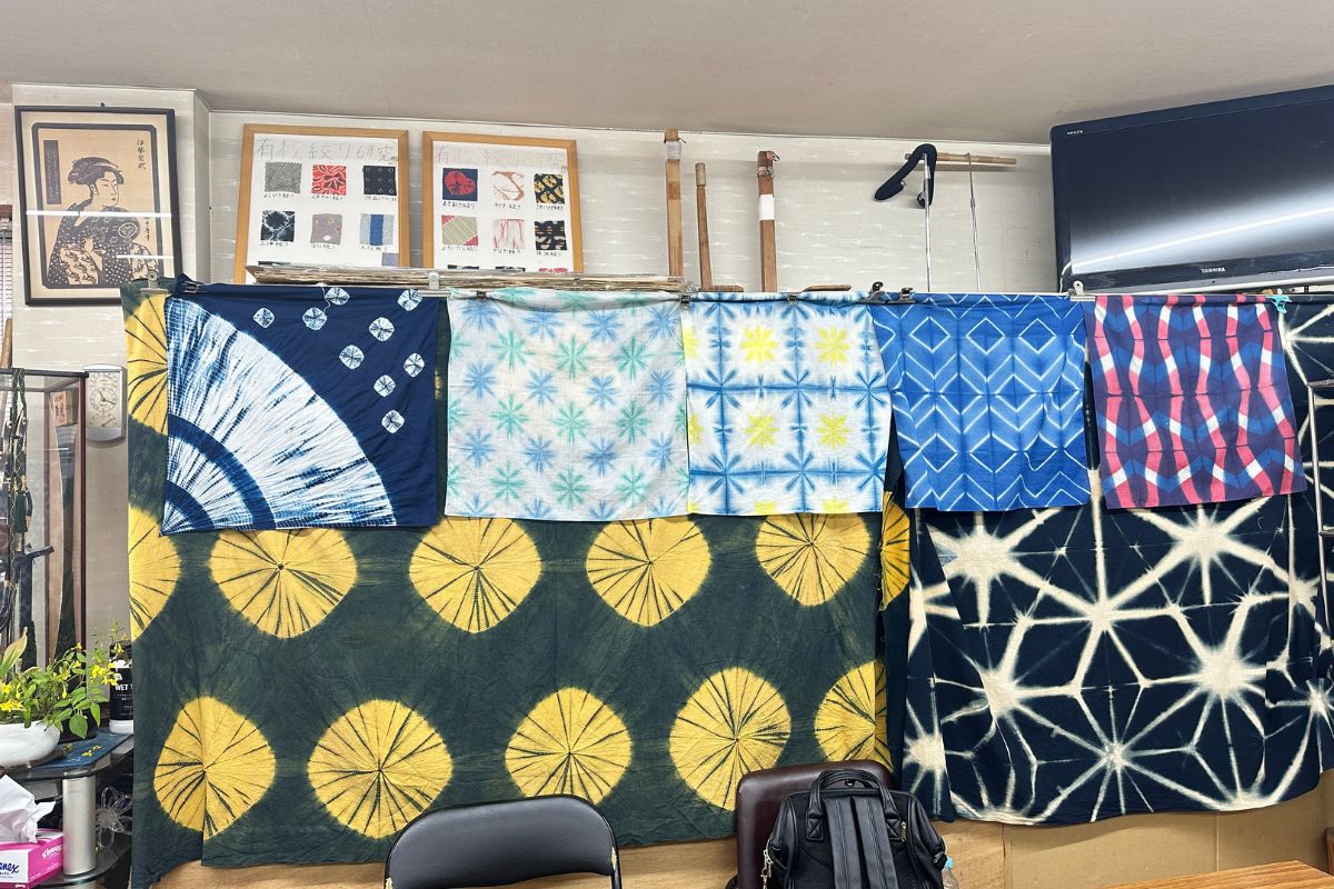 A display of dark blue and yellow geometric patterned cloths created using ancient folding techniques.