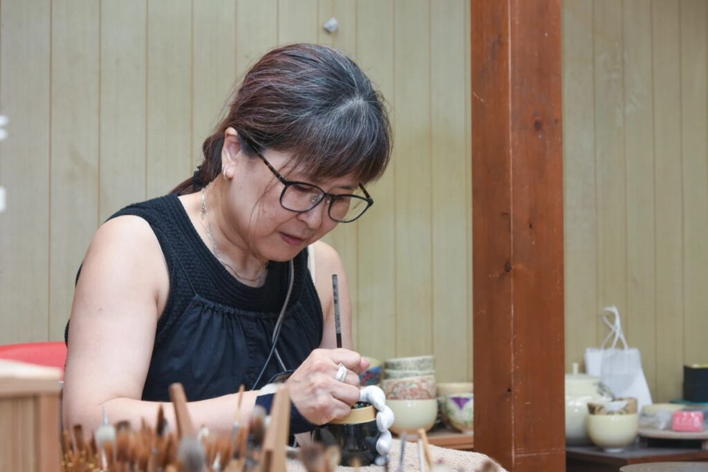 5th-generation master Maryu Sugita focusing on delicate ceramic painting inside her studio during the Kyoto pottery workshop experience.