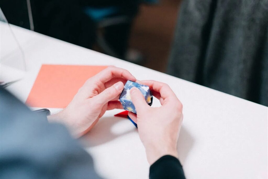 A detailed close-up of a participant's hands interlocking paper segments to build a complex geometric figure at a Tokyo origami private workshop.