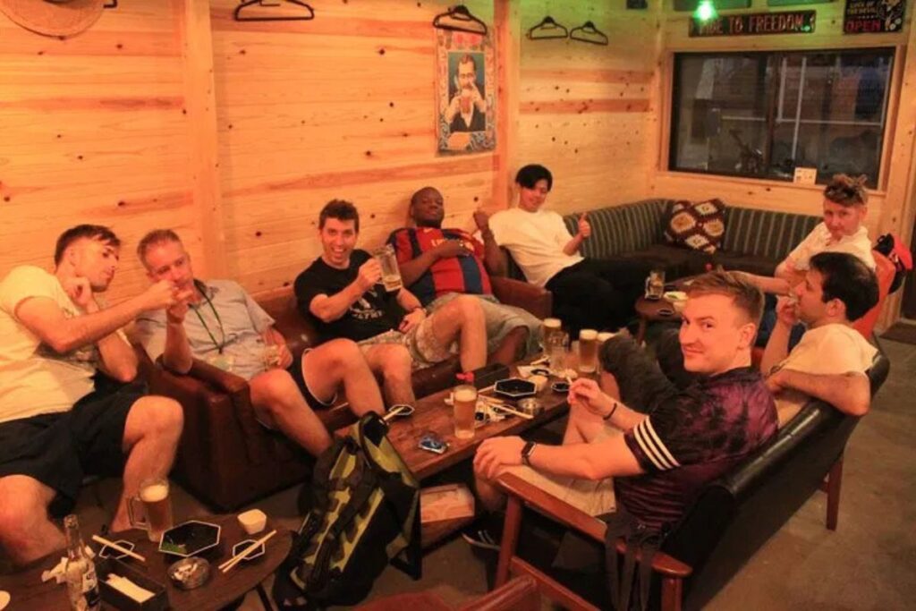 Travelers relaxing on comfortable couches inside a cozy neighborhood izakaya tavern.